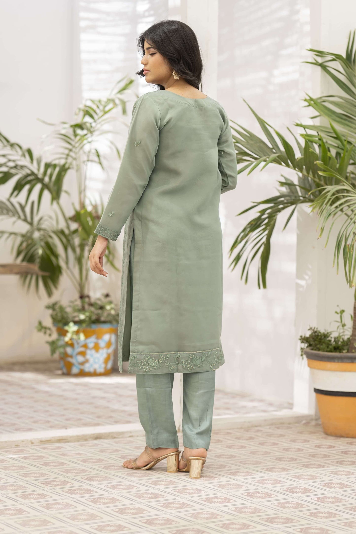 Woman wearing a light green traditional outfit in back side pose.