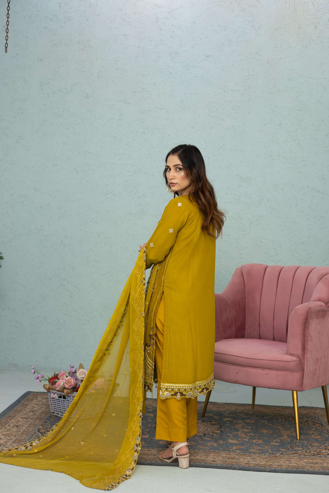 Woman in a light mustard traditional chiffon shalwar kameez outfit standing in a room back picture